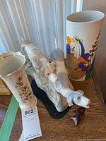 Photo showing porcelain figurine of two pointer dogs alongside two vases on a wooden surface