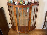 Front-right angled view of wooden china display cabinet with curved glass panels and single door, showing scratches and wear