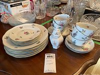 Porcelain china plates stacked with visible floral patterns and gold trim. Teacups and saucers are placed beside the plates. Visible cracks and chips on plates.