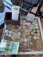 Photo showing a variety of different coins on a glass table along with a decorative metal box lined with red velvet.