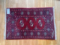 Full view of red rectangular hand pulled rug with geometric motifs and fringe edges, laid flat on wooden floor.