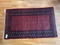 Full view of hand pulled oriental rug measuring approximately 35x23 inches laid flat on wooden floor showing overall pattern and white fringed tassels on shorter edges.