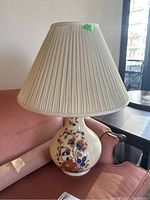 Full view of the ceramic table lamp with pleated fabric lampshade on a sofa.