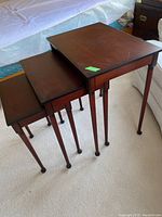 Full side view of three wooden nesting tables stacked, highlighting the tapered legs and brown finish.