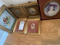 Six framed pictures displayed on floor including floral embroidery, four gold framed prints and one oval portrait with damaged frame