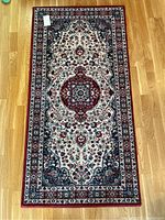 Full view of rectangular oriental-style rug on hardwood floor showing central medallion design and multiple decorative borders in burgundy, cream, and blue shades.