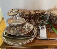 Tabletop display of silver-plated goblets, multiple trays, a scalloped bowl, candlestick holders, and an ice bucket, all showing tarnish.