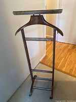 Front view of the entire wooden suit hanger showing the broad curved hanger arm, two horizontal crossbars, and wooden base on wheels.