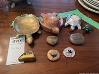 Photo showing brass turtle trinket bowl, carved wood turtle figurine, silver metal turtle candle holder, small green turtle figurine, and decorative stones with inscriptions and bird images.