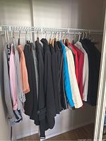 Long rack view showing a collection of women's jackets and tops hung neatly, ranging from light pinks and peaches to dark grays and blacks, plus some brighter colors.