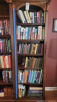 Full view of a wooden bookshelf packed with a variety of books, showing multiple shelves with different sizes and types of books.