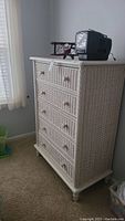 Front view of white wicker chest with five drawers and contents on top