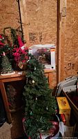 Photo of two artificial Christmas trees; one decorated with red bows and the other with ornaments and a Santa doll, along with pine cone trees and part of the holiday decor setup.