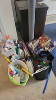 Cleaning supplies assortment in baskets and bags on floor including sprays, refill pads, cloths, and bottles.