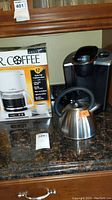 Photo showing Mr. Coffee drip coffee maker in box, Keurig coffee machine, and stainless steel kettle on countertop