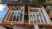 Drawer with two trays holding assorted flatware including knives, forks, spoons, and some with dark handles.