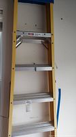Full view of the ladder showing yellow fiberglass frame, aluminum steps, and blue plastic top area demonstrating condition and materials.