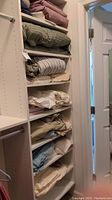 View of multiple folded sheets and pillowcases in various colors and patterns arranged on white shelving.