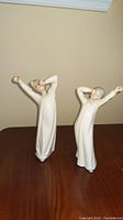 Two Lladro porcelain figurines standing side by side on a wooden surface.