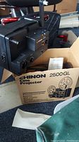 Chinon 2500GL projector with original box, film reel and instruction manual shown in garage setting.