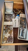 Drawer with assorted religious jewelry items including rosary, bracelets, crucifix, sterling silver bracelet box, and other small jewelry pieces.