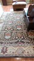 Full view of the wool rug with floral and geometric pattern on wood floor with furniture around