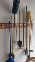 Tools hanging on wall-mounted rack in garage, showing brooms, mops, dusters, and a shovel among cleaning tools