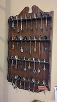 Full view of wooden display rack mounted on wall holding collection of souvenir spoons.