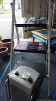 3 step ladder step stool with black steps and metal frame with DeLonghi heater placed on floor beneath it.