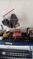 Photo of two remote control trucks and two remote control boats on a shelf. One boat is yellow, other white with rigging. Two trucks are red and brown, all with large tires and visible controllers in a plastic bag.