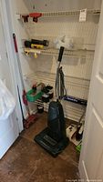Panasonic upright vacuum, push broom, dust pan, red Swiffer sweeper, and wire shelving with miscellaneous items
