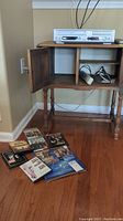 Sharp VHS/DVD combo player on wooden stand with remote and DVDs shown on floor