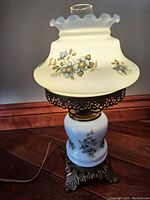 Full side view of the vintage hurricane lamp showing hand-painted blue floral designs on milk glass base and shade, brass ornamental base.