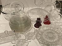 Several glassware plates, serving dishes, covered butter dish, sugar bowl and creamer arranged on a table showing varied patterns and styles.