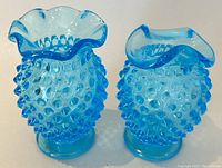 Pair of blue hobnail Fenton bud vases with scalloped open tops shown from front and angled views.