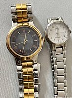 Two men's wristwatches side by side. The left watch has a two-tone gold and silver bracelet with a black dial and gold Roman numerals, identified as Seiko. The right watch is silver-tone with a white dial and Arabic numerals.