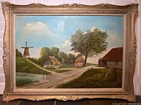 Framed oil painting showing rural Holland scenery with windmill, houses, and dirt path under a bright sky.