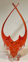 Front view of tall orange and clear art glass basket with stretched arching handles crossing at top.