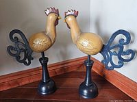 Pair of hand carved and painted wooden chickens, positioned facing each other showing front and side views, standing on hardwood floor.