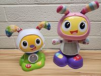 Two Fisher Price Bright Beats interactive toys, one pink and purple and one green and white, showing fronts and sides with detail on light-up buttons and antennae