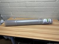 Rolled up heavy duty office mat placed on a wooden surface against a brick wall background, showing full length and thickness.