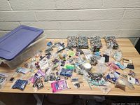Overview of the large assortment of beads, small jewelry findings, and plastic storage bin on a table.