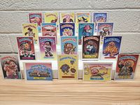 Front view of 12 Garbage Pail Kids cards arranged in 2 rows showing various characters with colorful backgrounds and character names.