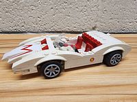 White and red LEGO Mach 5 car from Speed Racer, side angle showing decals and wheel detail on wooden surface.