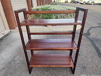 Front view of wood folding shelf showing four wooden shelves with side panels and a dark finish.