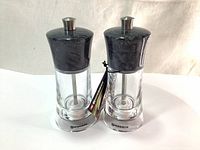 Two Swissmar Granite mills with clear acrylic bodies and granite textured tops standing upright, showing front and side.