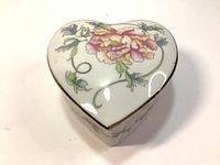 Heart-shaped ceramic trinket box with floral hand-painted decoration on the lid, showing pink and yellow peony flowers and green leaves.