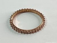 Rose gold-tone eternity ring with clear stones arranged around entire band, laying flat on white surface.