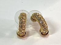 Close up photo of the pair of Swarovski half hoop gold tone earrings with clear crystal embellishments and plastic backs