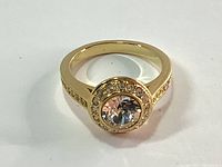 Front view of gold tone ring with large round Swarovski crystal and pavé halo setting on band.